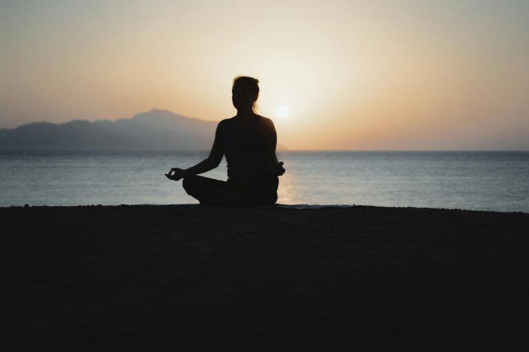 Prayer - Spirits Energy Inc. A woman practices meditation with a tranquil ocean sunset backdrop, embodying peace and relaxation.